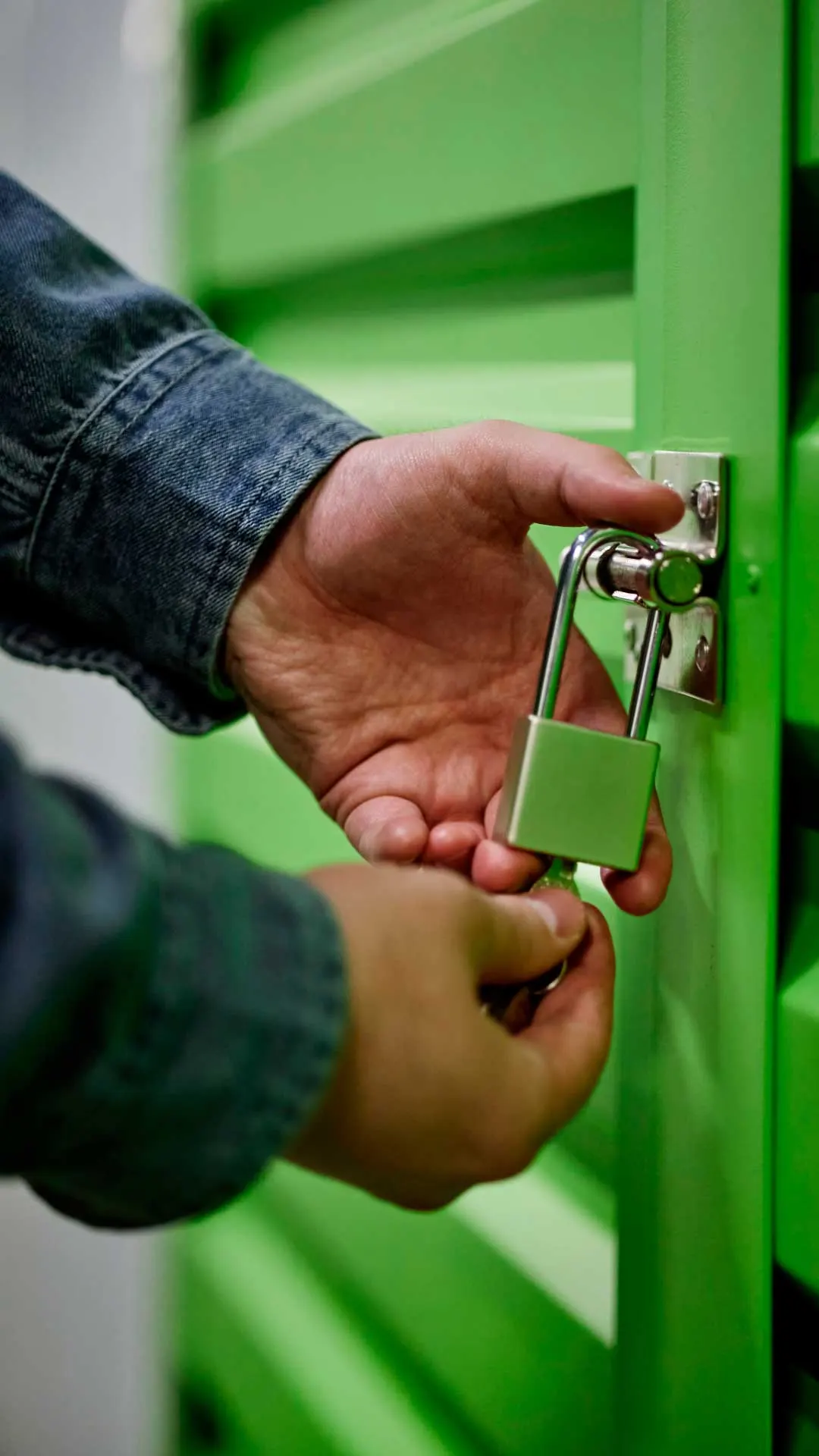 Mano cerrando con candado un trastero de puerta verde